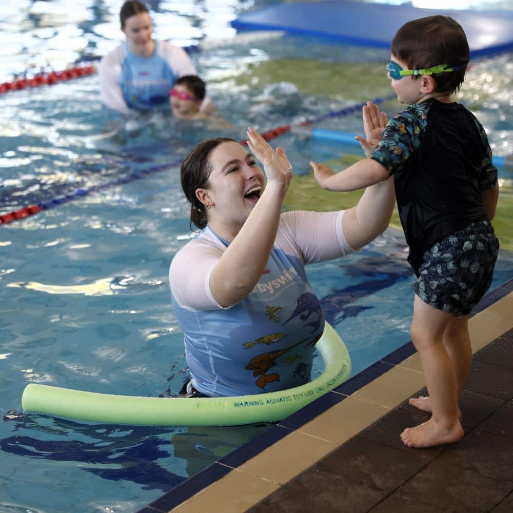 A mother inside the Kirby Swim Swimming Pool is playing with her son that is standing outside the pool 1000 x 1000